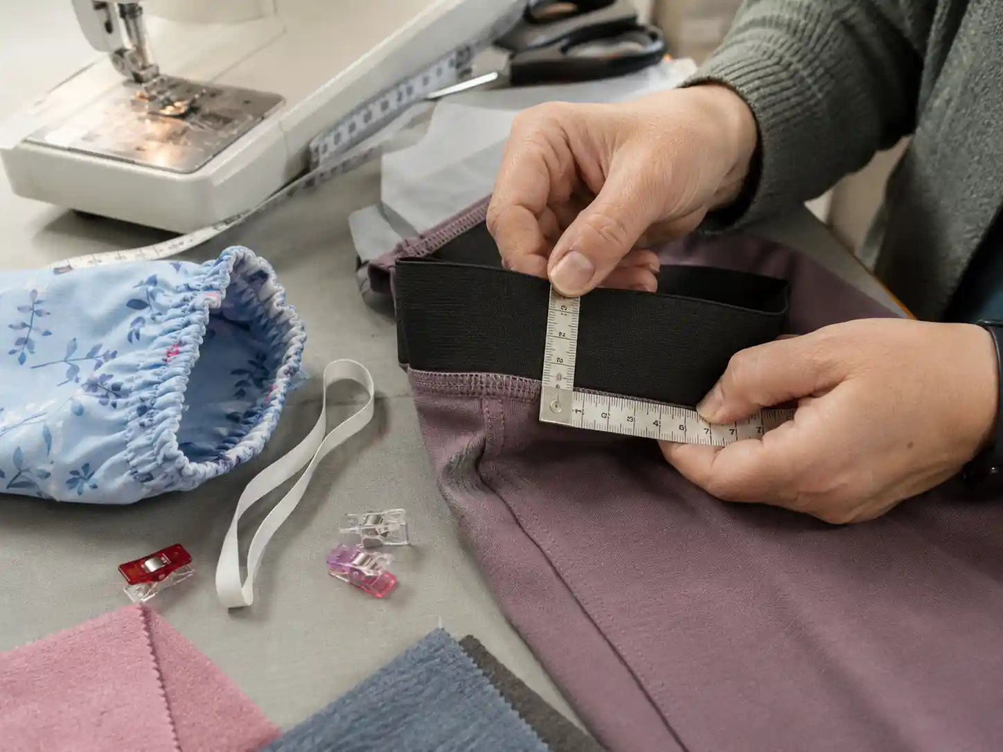 Hands measuring wide elastic on a garment waistband.